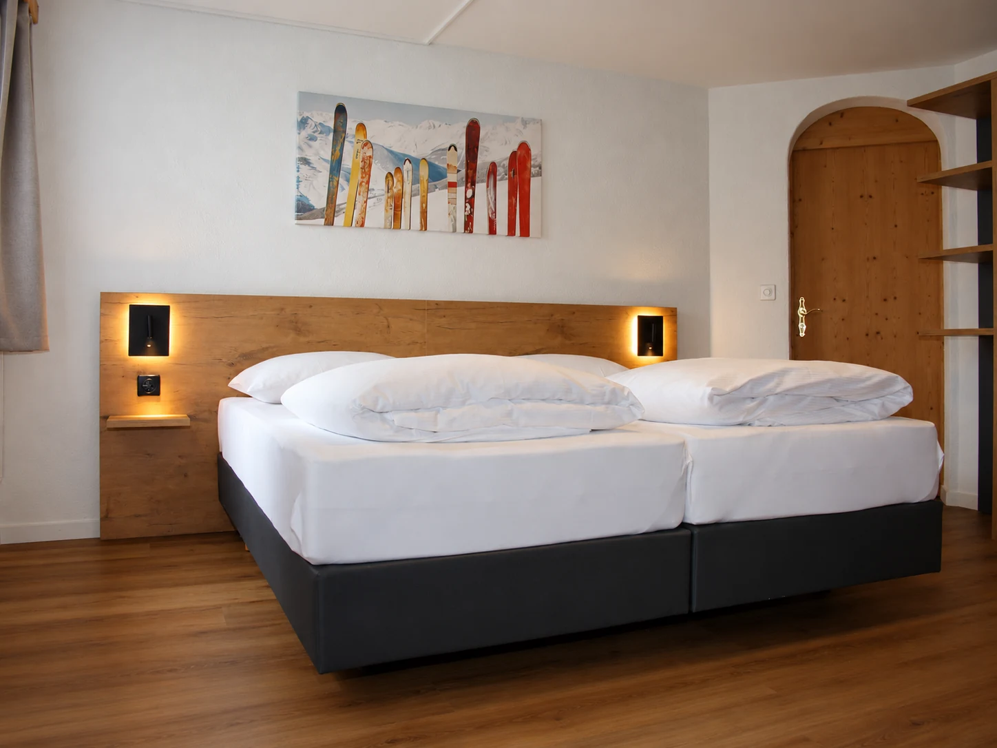 Zweibettzimmer mit Holzboden und buntem Skimotiv über dem Bett