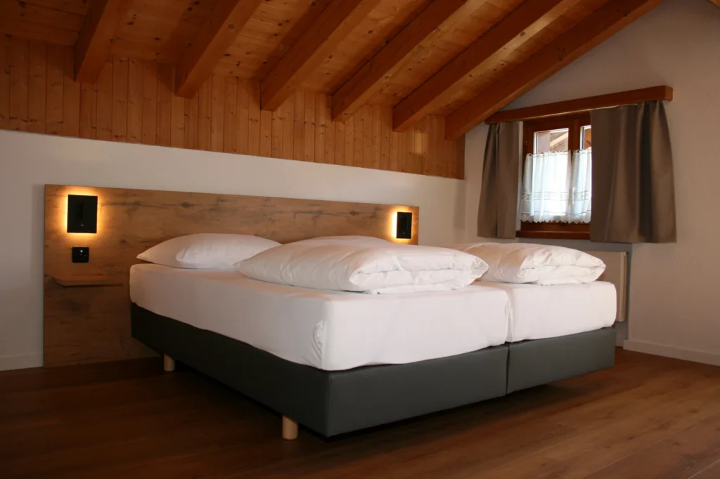Zimmer im Dachgeschoss mit sichtbaren Holzbalken und Doppelbett