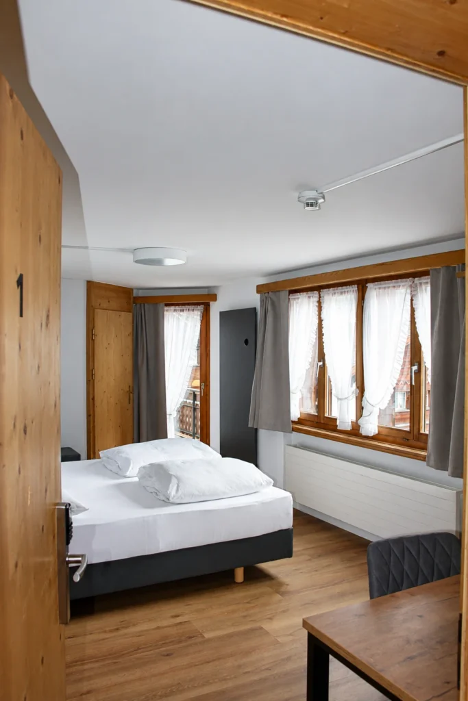 Blick durch die Holztür auf ein helles Zimmer mit grossen Fenstern