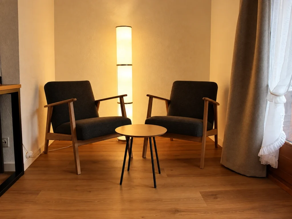 Zwei Sessel mit rundem Tisch und warmer Stehleuchte am Fenster